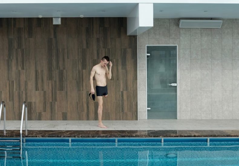 Amputee athlete preparing at an indoor swimming pool, portraying determination and fitness.